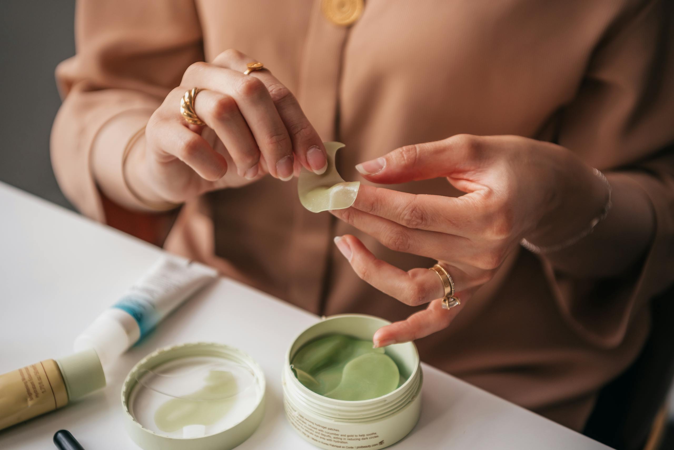 Close-up of Woman Holding an Under Eye Patch and Sitting at a Table with Cosmetics